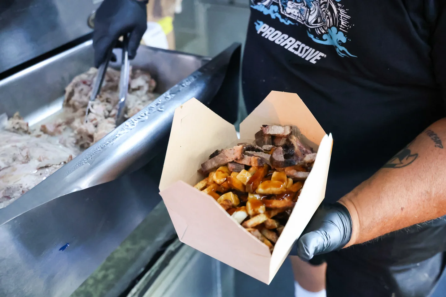 Pulled pork poutine being plated with tongs from service line