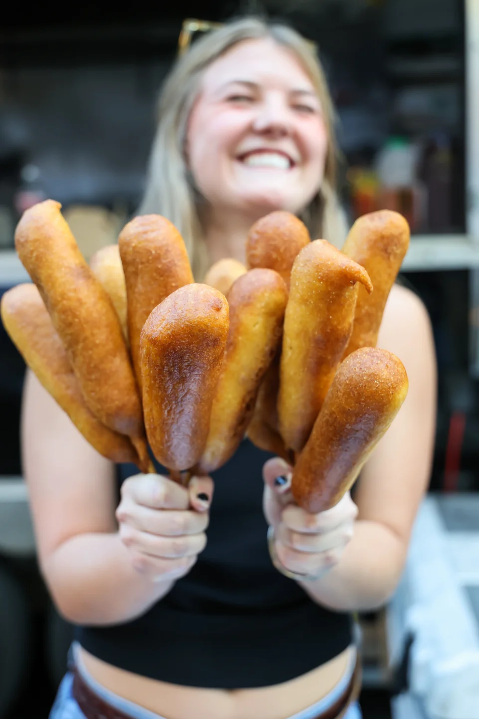 Woman smiling, holding a full bouquet of corndogs on sticks