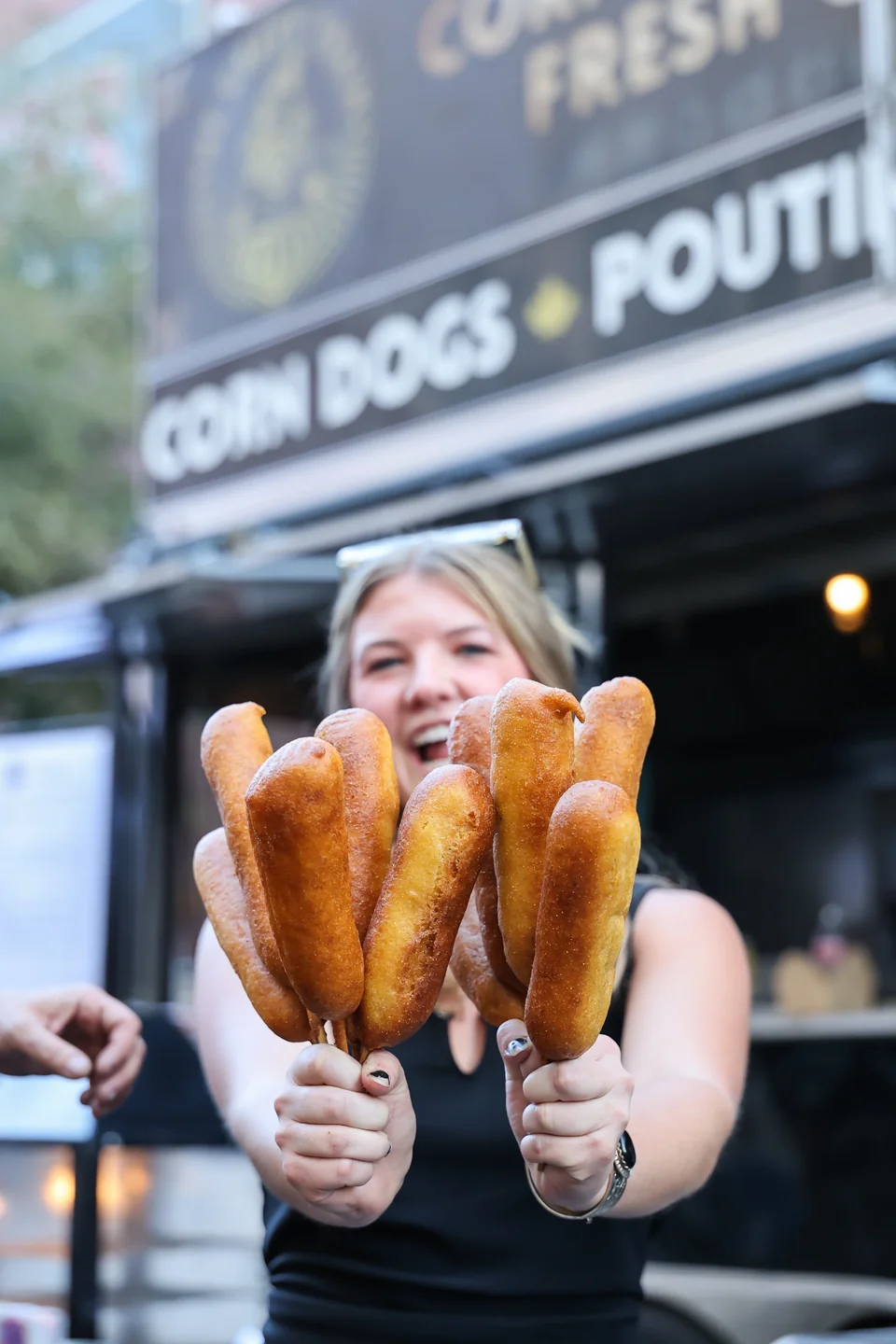 Woman holding corndogs in front of The Gravy Train truck at evening