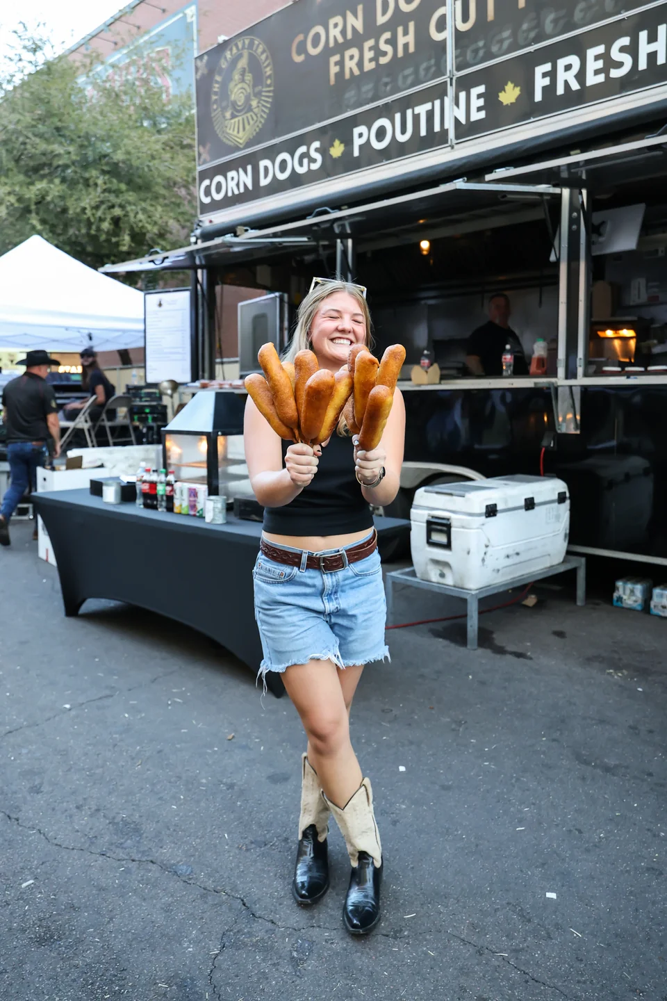 Woman holding corndogs in front of The Gravy Train truck in daytime