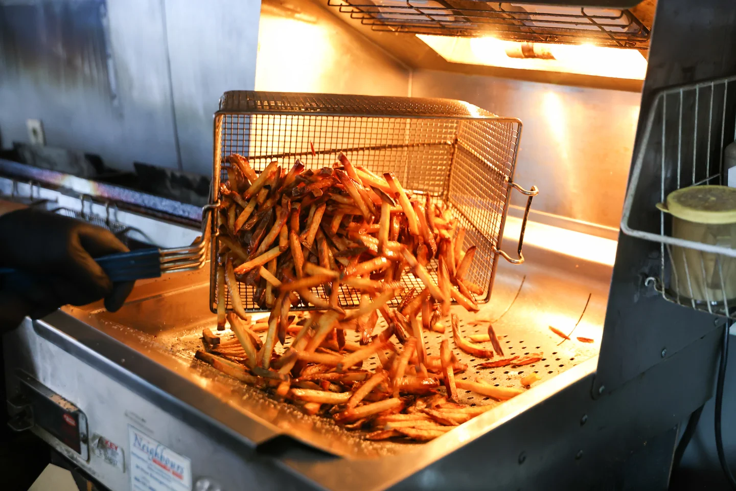 Fresh-cut fries tumbling from a fryer basket under warm light